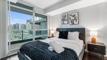 A modern hotel room with a large bed, a city view, and two framed floral artworks on the wall.