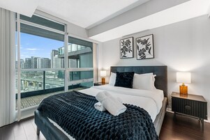 A modern hotel room with a large bed, a city view, and two framed floral artworks on the wall.