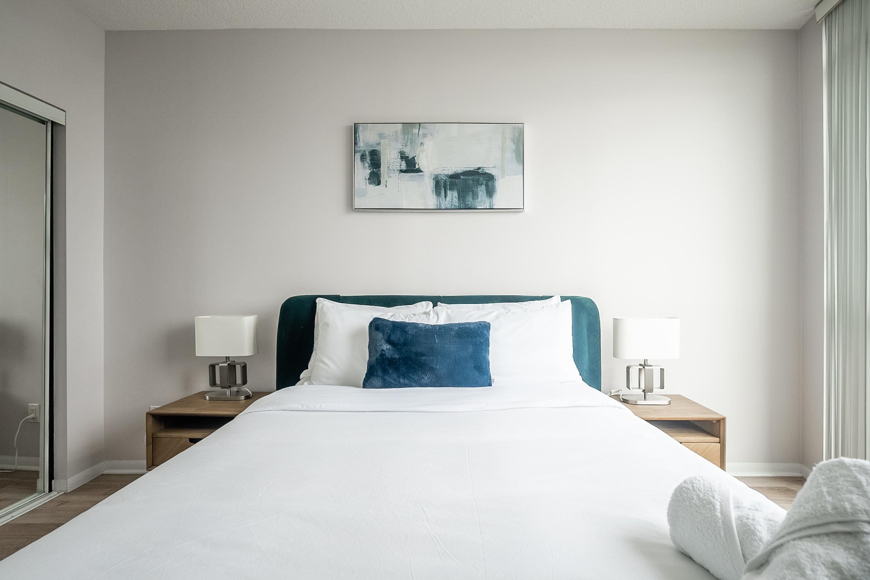 Een hotelkamer met een bed, twee nachtkastjes met lampen, een bijzettafeltje, een schilderij aan de muur en een raam.