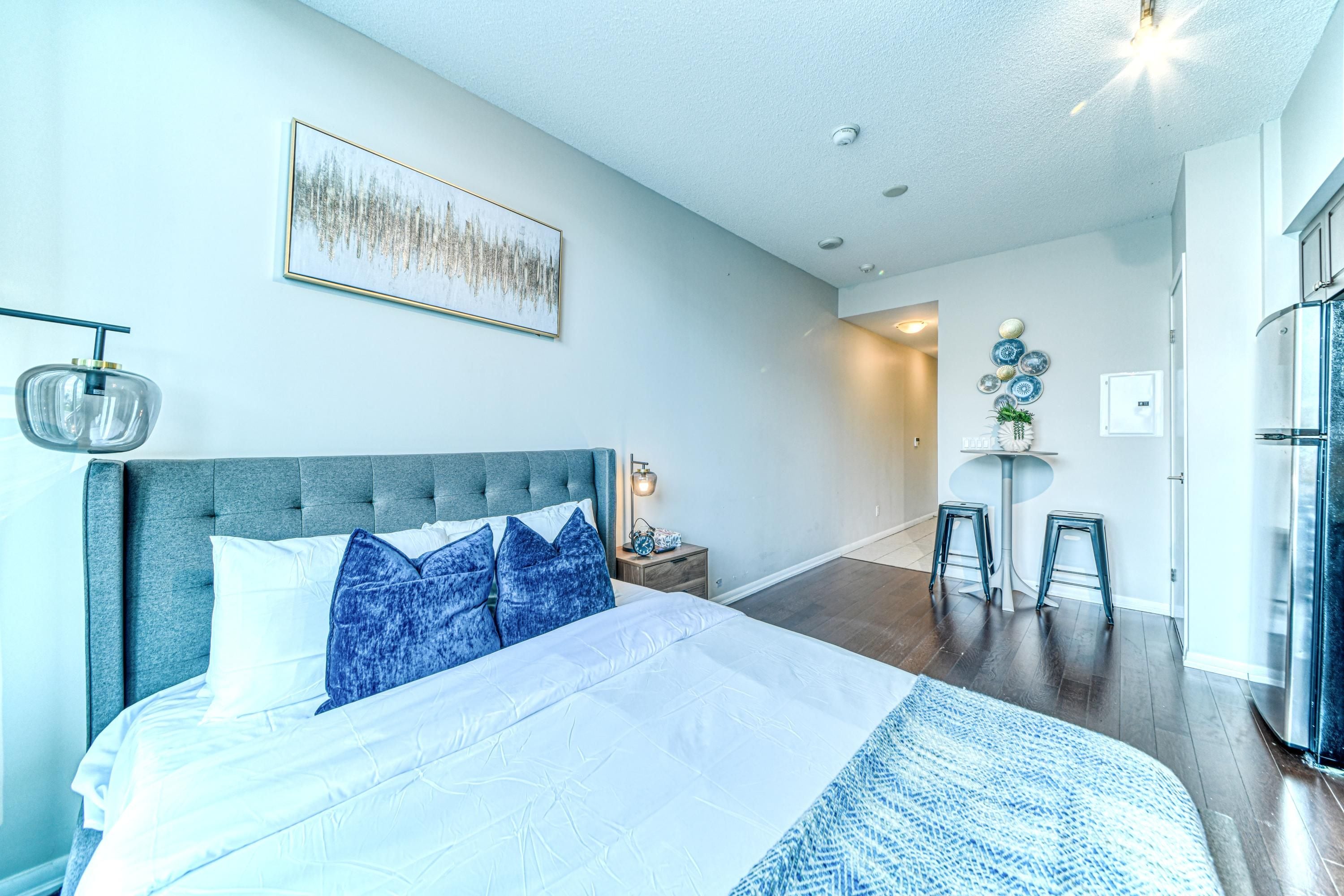 Een slaapkamer met een bed, een nachtkastje, een wandlamp, een lijst met een afbeelding en een zithoek met krukken.