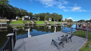 A wooden deck with two chairs overlooking a calm water body, surrounded by greenery and a clear sky. - Waterfront RV Oasis: Dock & Pavilion | Lot 561 (River Ranch)