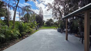 A covered outdoor area with a concrete floor, surrounded by lush greenery and trees.