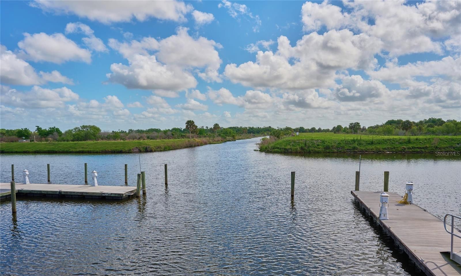 Une rivière paisible, avec une jetée en bois sur la rive gauche et une berge herbeuse sur la rive droite.
