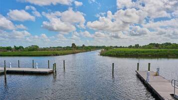 Une rivière paisible, avec une jetée en bois sur la rive gauche et une berge herbeuse sur la rive droite.