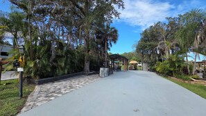 A paved driveway leading to a covered outdoor area with a gazebo, surrounded by lush greenery and trees.