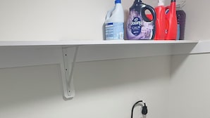 A laundry area with two Whirlpool washers, a shelf with cleaning products, and a power outlet. -     Brand-New Luxury Home Spacious, Stylish & Your Home Away From Home (Tobyhanna)