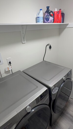 Een wasruimte met twee Whirlpool wasmachines, een plank met schoonmaakmiddelen en een stopcontact.
