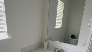 A bathroom with a white sink, a mirror, and a window with blinds. -     Brand-New Luxury Home Spacious, Stylish & Your Home Away From Home (Tobyhanna)