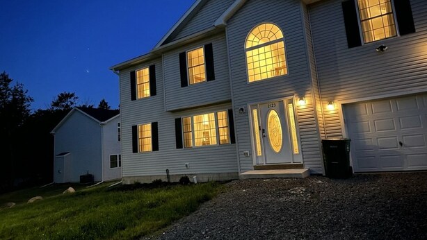 A two-story house with a garage, a driveway, and a well-lit front door. -     Brand-New Luxury Home Spacious, Stylish & Your Home Away From Home (Tobyhanna)