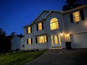 Een twee verdiepingen tellend huis met een garage, oprit en een goed verlichte voordeur.