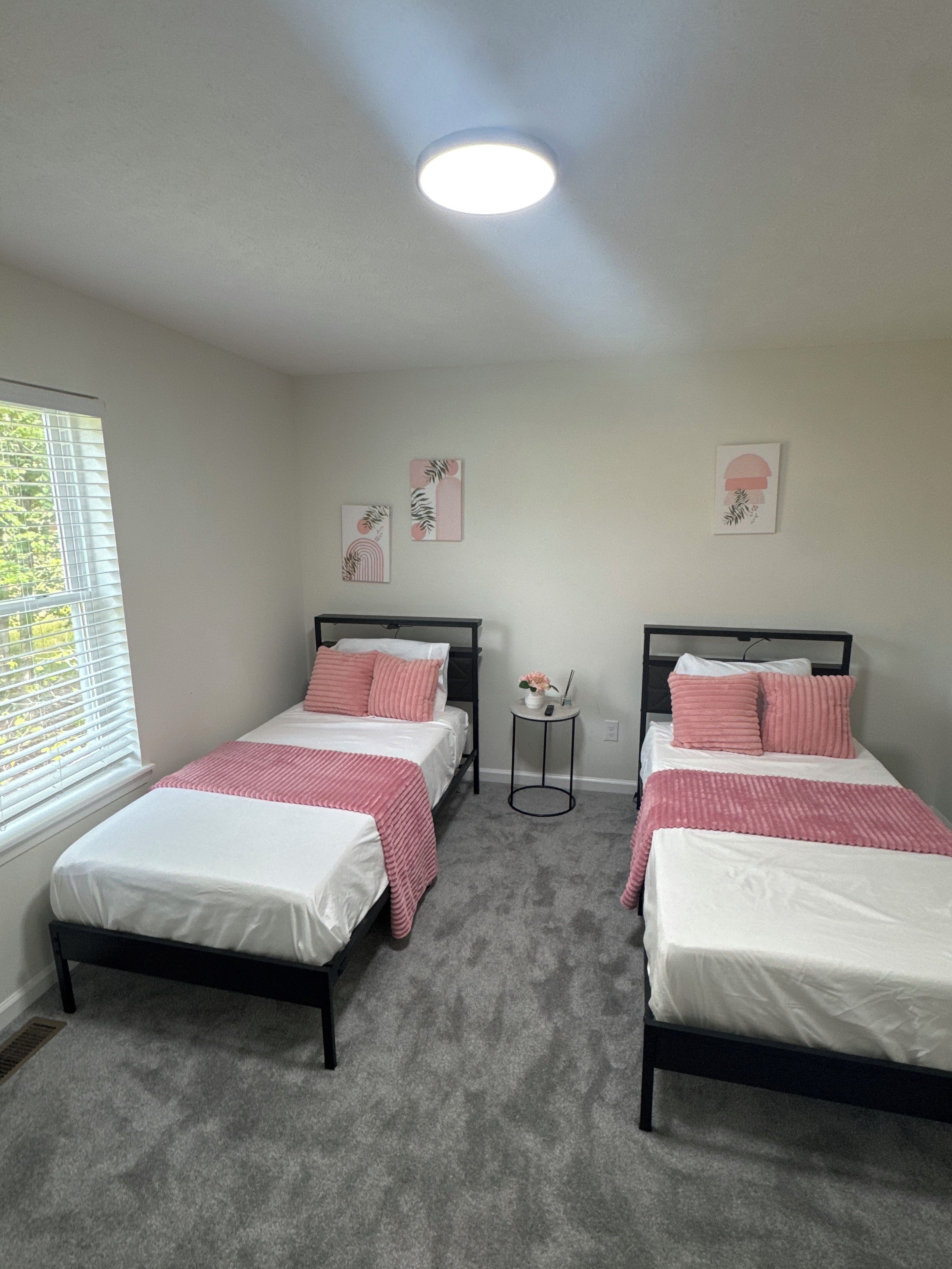 A bedroom with two beds, a window with blinds, and a ceiling light.