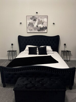 A bedroom with a tufted headboard, a black upholstered bench, two bedside tables with lamps, and a framed abstract painting on the wall. -     Brand-New Luxury Home Spacious, Stylish & Your Home Away From Home (Tobyhanna)