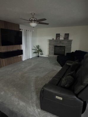 A living room with a flat-screen TV, a fireplace, a ceiling fan, and a dark-colored sofa. -     Brand-New Luxury Home Spacious, Stylish & Your Home Away From Home (Tobyhanna)