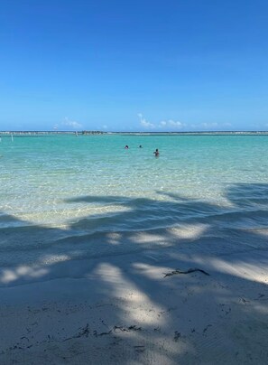 En strand med klart turkis vand, en sandstrand og en fjerndragen mole.