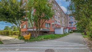 Edificio residencial con entrada pavimentada y un contenedor amarillo para basura.