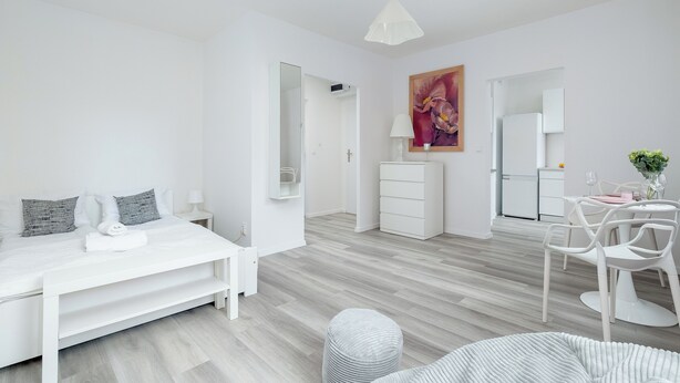 Un dormitorio moderno y minimalista con cama, mesitas de noche, cómoda y un área de comedor con sillas y una mesa.