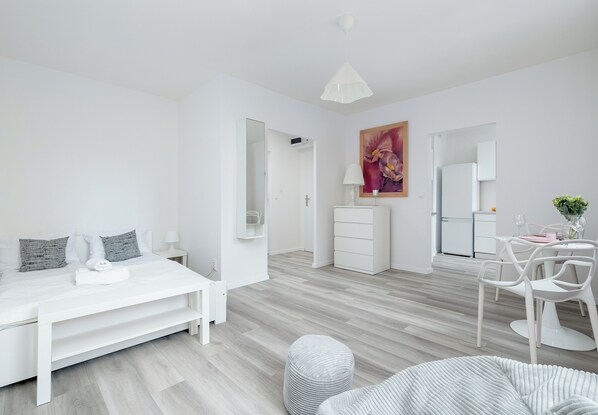 Een moderne, minimalistisch ingerichte slaapkamer met een bed, nachtkastjes, een dressoir en een zithoek met stoelen en een tafel.
