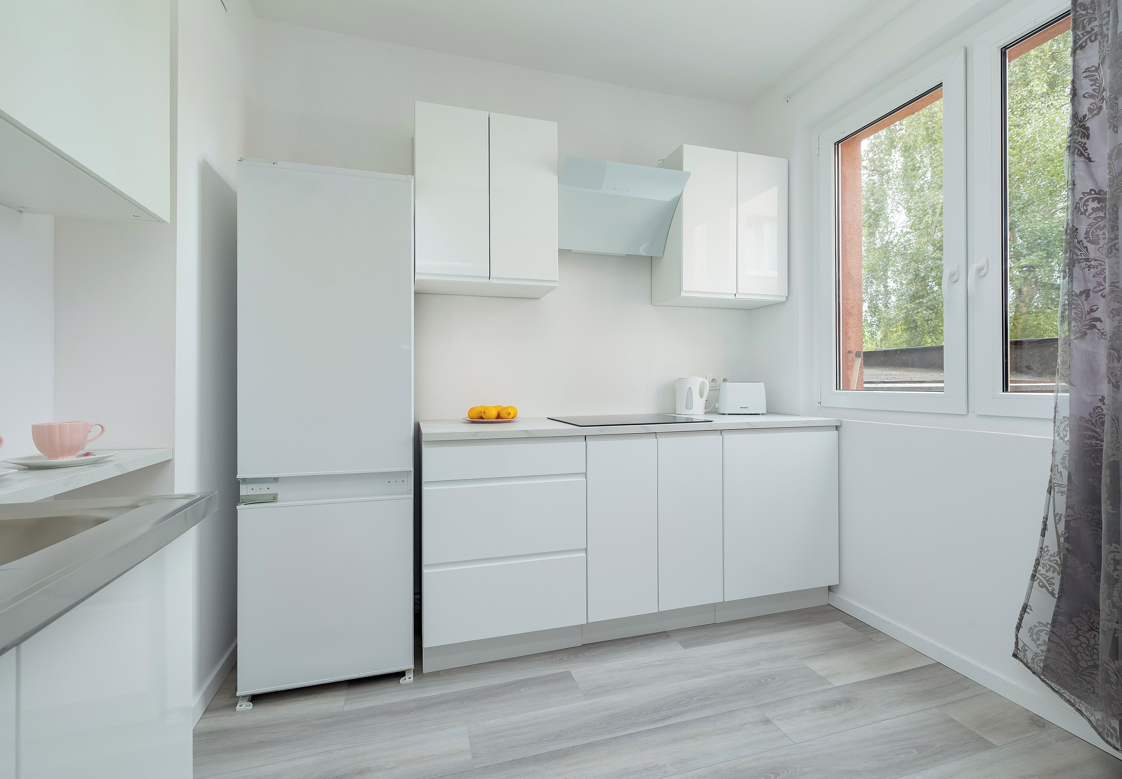 A compact kitchen with white cabinets, a built-in microwave, and a window with a view of greenery.
