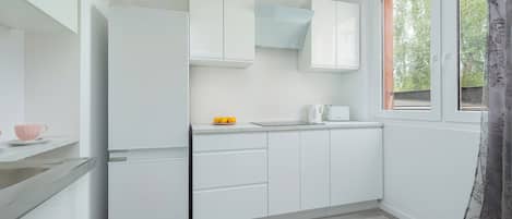 Une cuisine compacte avec des meubles blancs, un four à micro-ondes encastré et une fenêtre donnant sur un espace verdoyant.