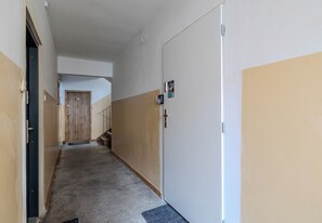 Ein Korridor mit einer Holztür am Ende, einer weißen Tür mit einem QR-Code und einer Treppe.