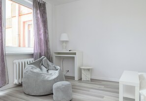 Ein schlicht eingerichteter Raum mit Heizkörper, weißem Schreibtisch, Lampe, Sitzsack und kleinem Tisch.