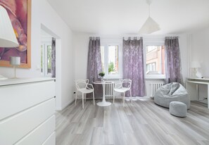 A modern, well-lit room with a dining area, two chairs, a table, a sofa, and a large window with curtains. - Szczecin Boryny Blossom Studio (Szczecin)