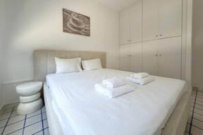 A hotel room with a bed, a wardrobe, and a wall-mounted artwork. - Modern 2BR Beach Retreat at Harmony (Germasogeia)