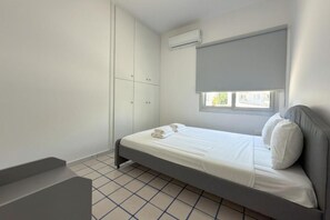 A bedroom with a bed, a wardrobe, an air conditioning unit, and a window with a blind. - Modern 2BR Beach Retreat at Harmony (Germasogeia)