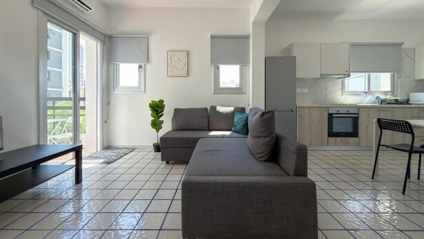 Un salon moderne avec un canapé d’angle gris, une petite table et une plante en pot.