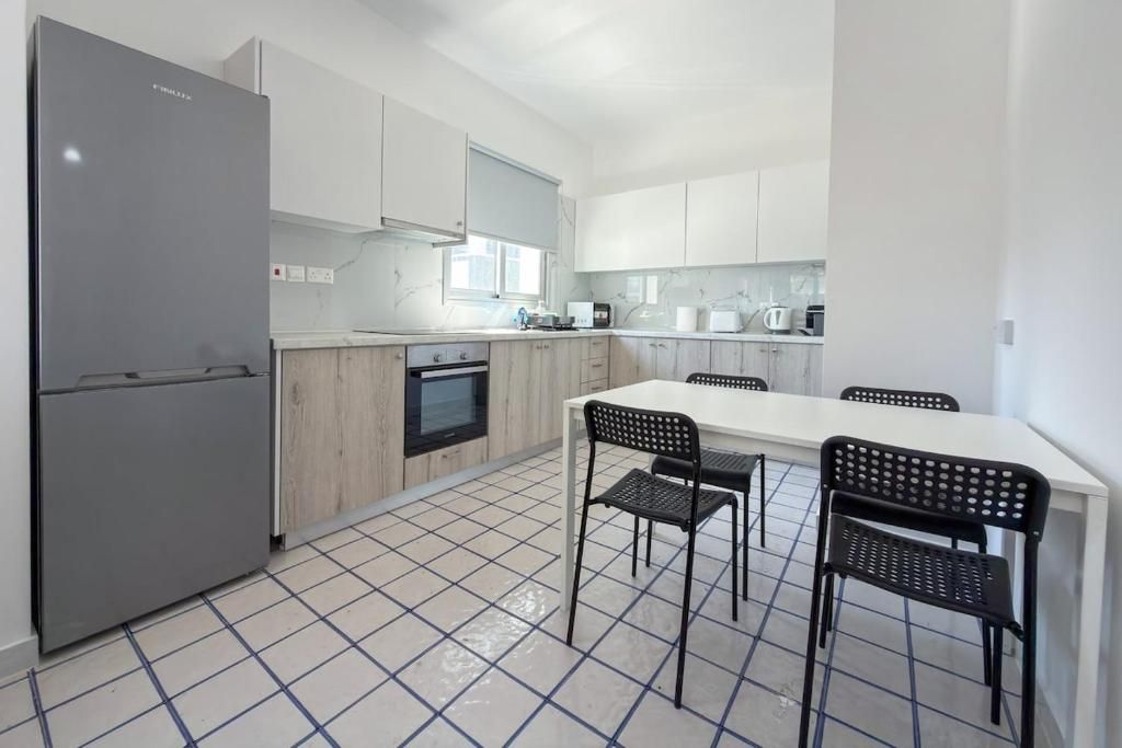 Une cuisine moderne équipée d’un réfrigérateur, d’un four et de meubles blancs. On y trouve également une table à manger avec des chaises.