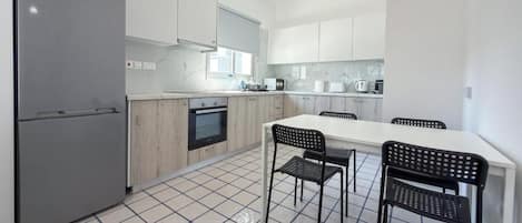 A modern kitchen with a refrigerator, oven, and white cabinets. There is a dining table with chairs.