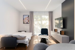 A modern hotel room with a bed, a desk, a chair, a TV, and a painting on the wall. - Portowa Riverfront Apartment (Kraków)