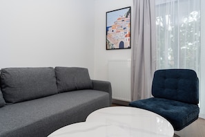 Ett vardagsrum med en grå soffa, en blå fåtölj och ett vitt soffbord.