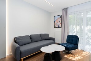 Ein modernes Wohnzimmer mit einem grauen Sofa, einem blauen Sessel und einem weißen runden Tisch.