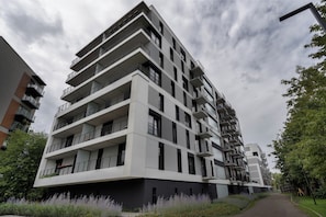En flervåningsbyggnad med bostäder, balkonger, en modern arkitektonisk design och en gångväg som leder till entrén.