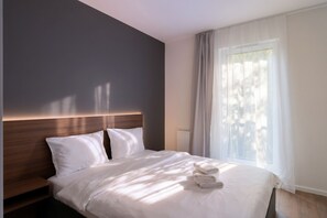 Une chambre d’hôtel avec un lit, une table de chevet, une fenêtre avec des rideaux légers et un radiateur.