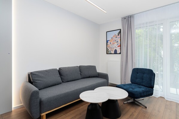 Ett modernt vardagsrum med en grå soffa, en blå fåtölj och ett vitt, runt bord.