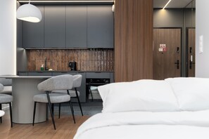 Ein modernes Hotelzimmer mit einem Bett, einer kleinen Küchenzeile und einer Sitzecke mit Stühlen.