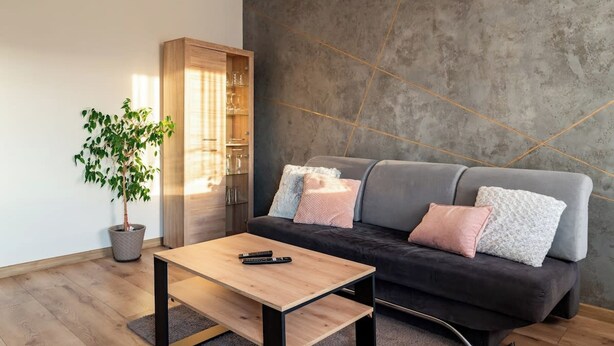 Een moderne woonkamer met een grijze bank, een houten salontafel en een potplant.