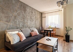 A modern living room with a grey sofa, a wooden coffee table, and a dining area with a table and chairs. - Gdańsk Burzyńskiego Cozy Stay Apartment (Gdańsk)