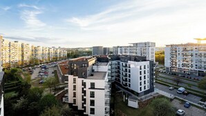 Een hoog appartementencomplex met meerdere balkons, een parkeerplaats en een helder uitzicht over het omliggende stadslandschap.