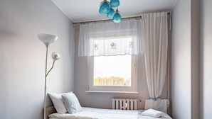 Ein Schlafzimmer mit einem Einzelbett, einem Nachttisch, einer Lampe und einem Fenster mit Vorhängen.