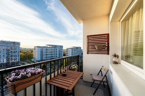 A balcony with a wooden table, a chair, a hanging flower basket, and a window with blinds. - Gdańsk Burzyńskiego Cozy Stay Apartment (Gdańsk)