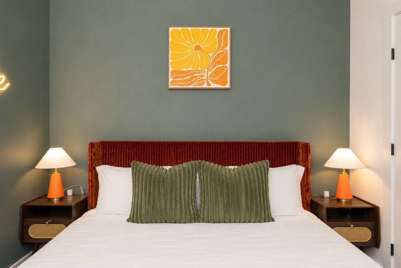 A bed with a red headboard, two bedside lamps, a green pillow, and a wall art piece.