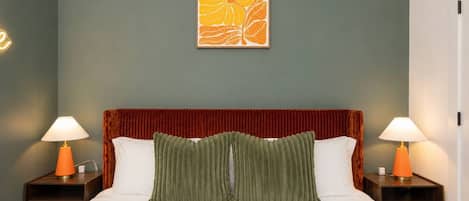 A bed with a red headboard, two bedside lamps, a green pillow, and a wall art piece.