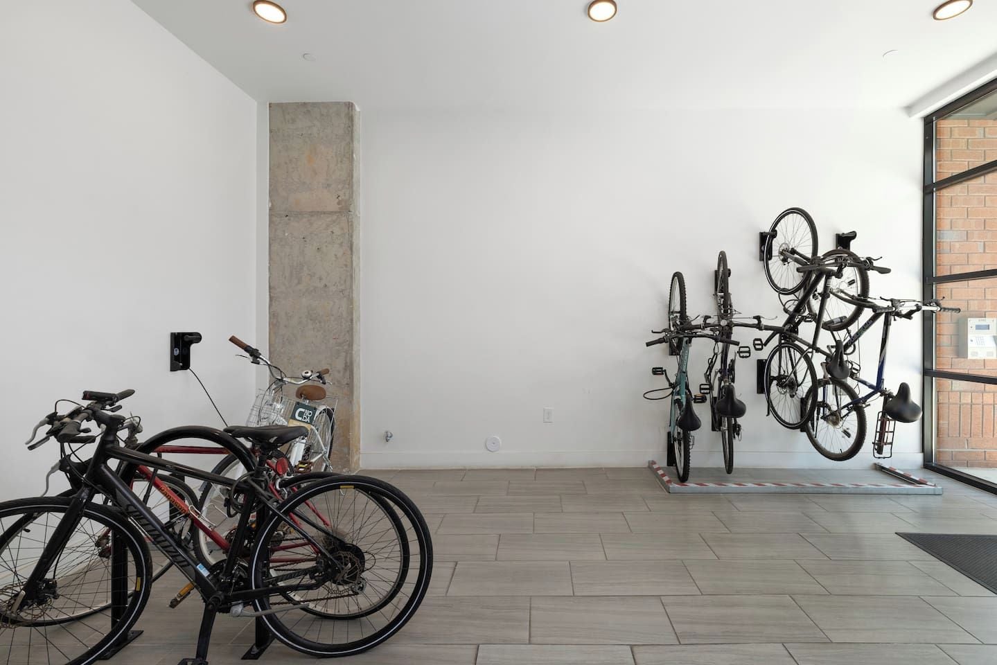 A room with bicycles parked against the wall, a concrete pillar, and a door leading outside.