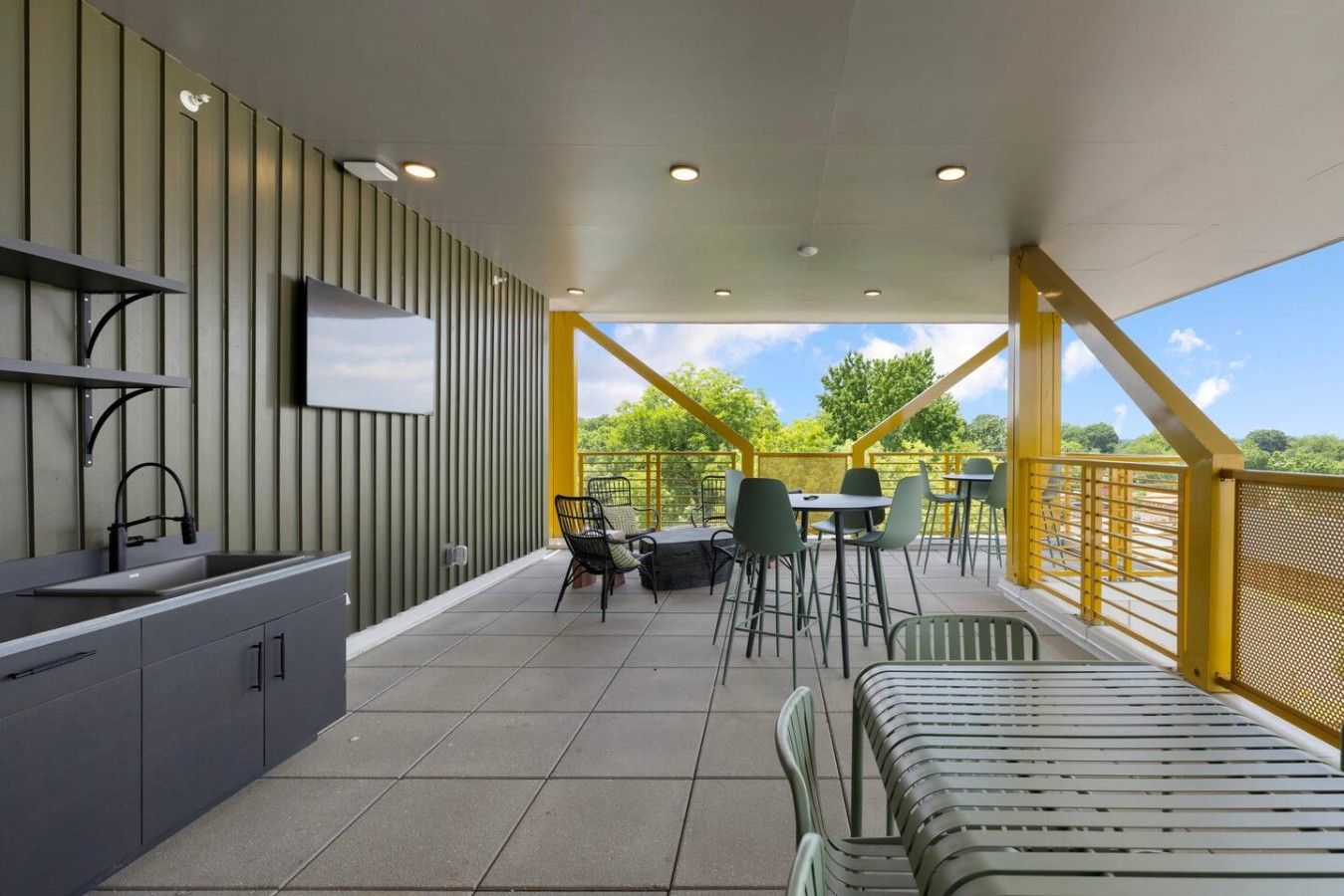 Un espacio moderno al aire libre con zona de comedor, mostrador de cocina, sillas y televisor montado en la pared.