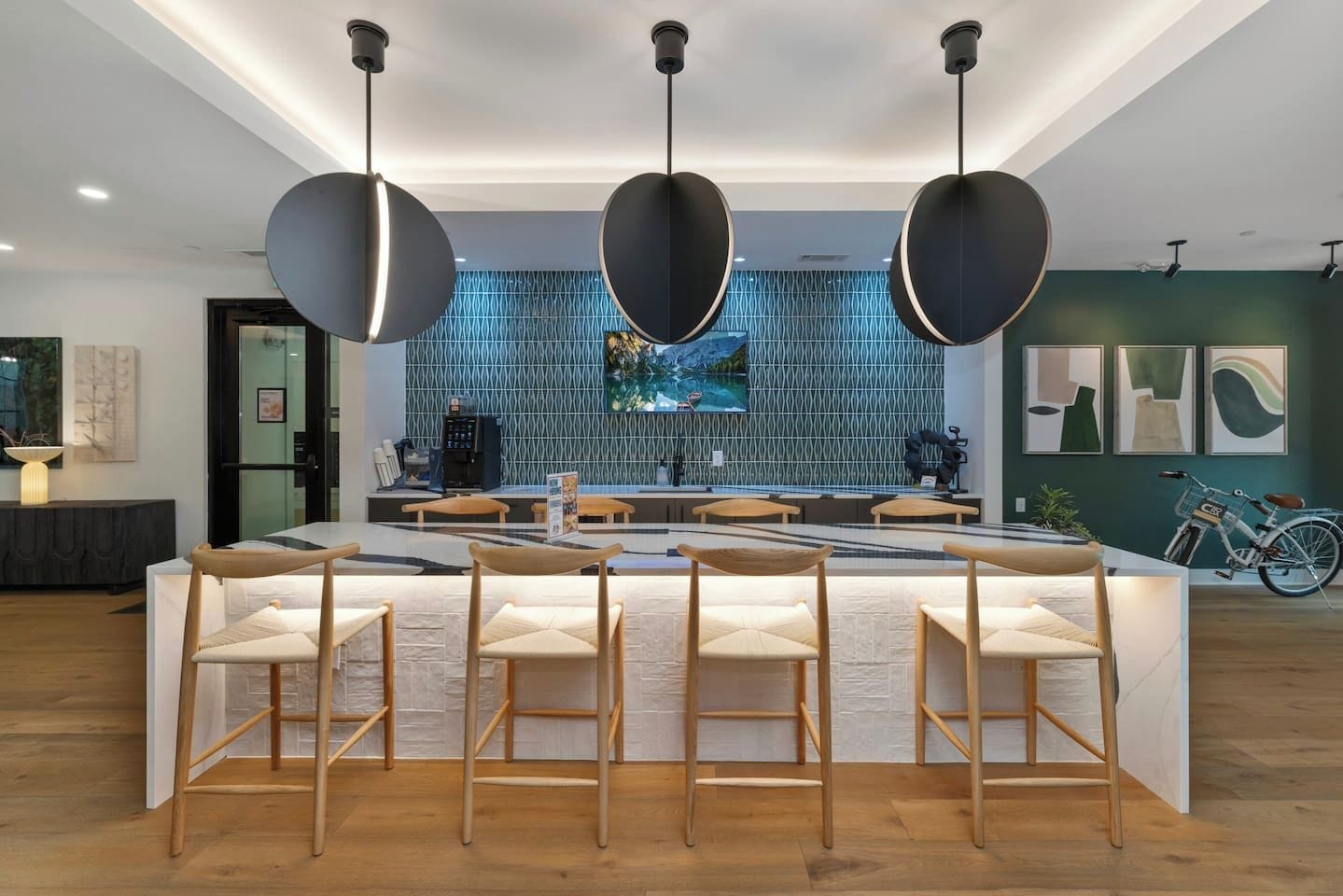A modern bar area with a central island, bar stools, pendant lighting, and a patterned wall.