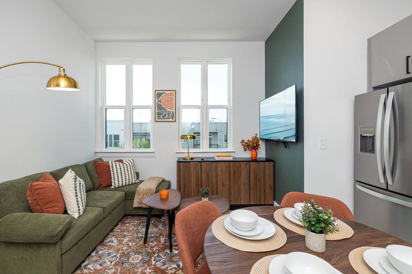A modern living room with a green sofa, a coffee table, and a dining area with a wooden table set for two.