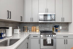 Une cuisine moderne avec des meubles gris, un four à micro-ondes en acier inoxydable, une cuisinière à gaz et un four encastré.
